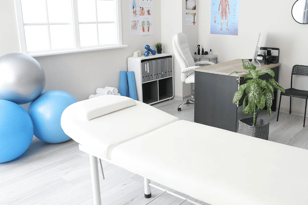 Physiotherapie Wittenberg Praxis Behandlungsraum mit Liege, Schreibtisch, Pflanzen und blauen Gymnastikbällen.