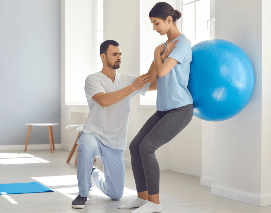 Physiotherapeut Lutherstadt Wittenberg Gymnastikball Ein Trainer unterstützt eine Frau bei einer Übung mit einem großen Gymnastikball.